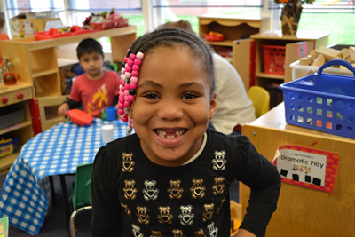 A little girl who is missing some front teeth and smiling at the camera.