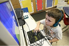 Photo of young boy wearing headphones and working at a computer.