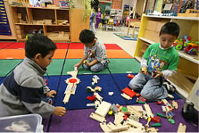 Photo of three boys playing with wooden train tracks