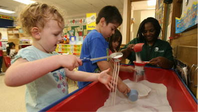Photo of several children playing together around a large sandbox