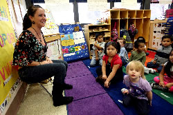 Photo of teacher sitting in front of class of students who are sitting on the floor